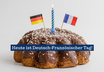 Foto eines Kuchens. Auf dem Kuchen steckt eine brennende Kerze und je eine Flagge Deutschlands und Frankreichs. &Uuml;ber den Kuchen l&auml;uft der Schriftzug "Heute ist Deutsch-Franz&ouml;sischer Tag!".