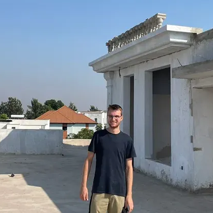 Nico steht auf einer Baustelle. Um ihn herum ist viel grauer Beton. Er blickt in die Kamera.