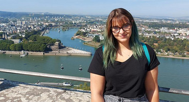 Foto: Anastassia trägt ein schwarzes Tshirt und lehnt an einem Betongeländer, im Hintergrund sieht man den Ohrid See von oben