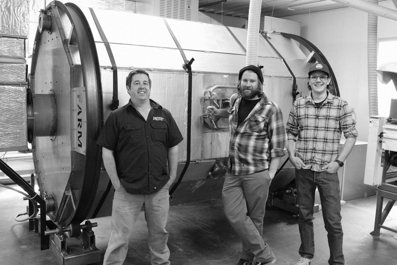 Foto: drei Männer stehen vor einem großen Metalltank und lächeln in die Kamera