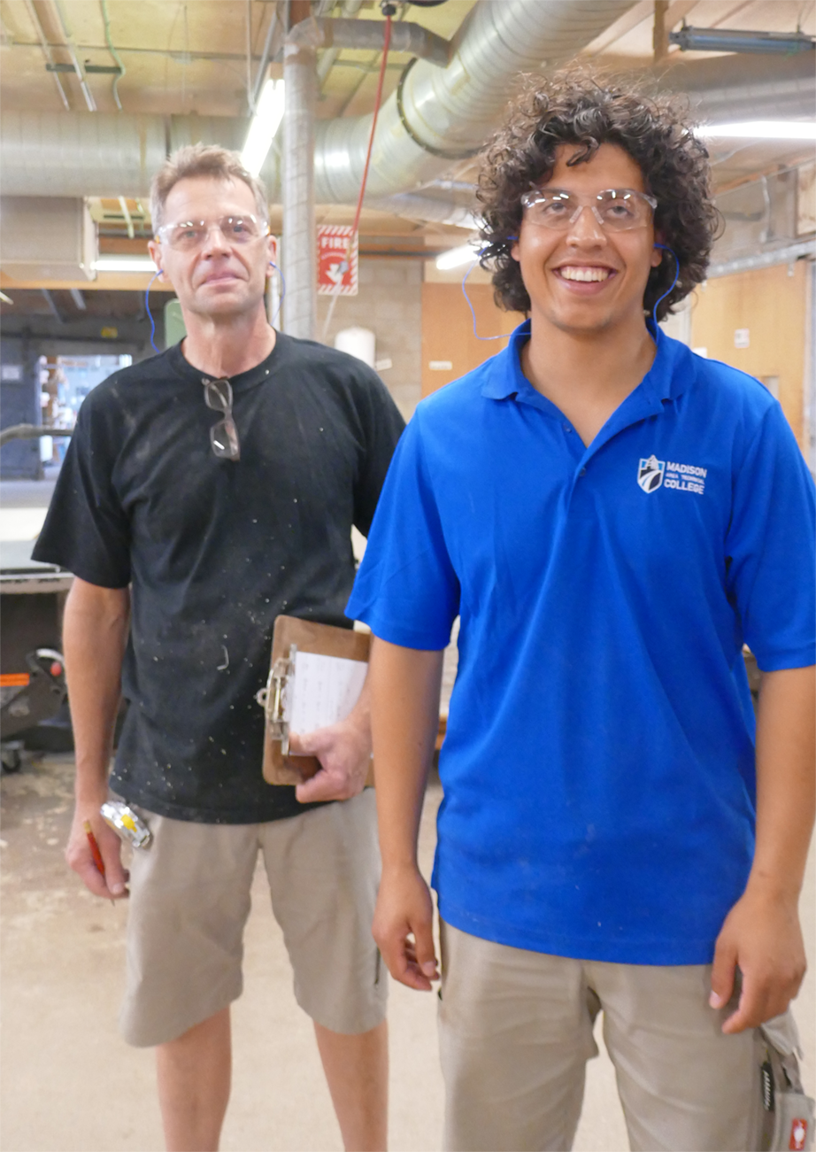 Foto: Keanu steht mit einem Kollegen im Betrieb und beide lächeln in die Kamera