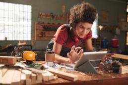 Foto: eine junge Schreinerin in der Werkstatt klickt auf dem Tablet.