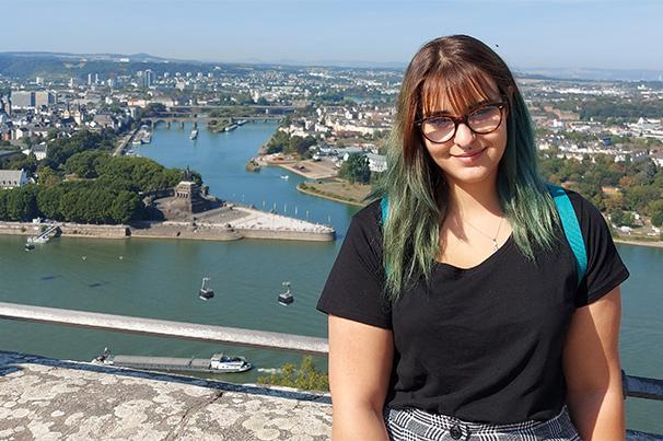 Foto: junge Frau mit schwarzem Tshirt blickt in die Kamera, im Hintergrund blaugrünes Wasser