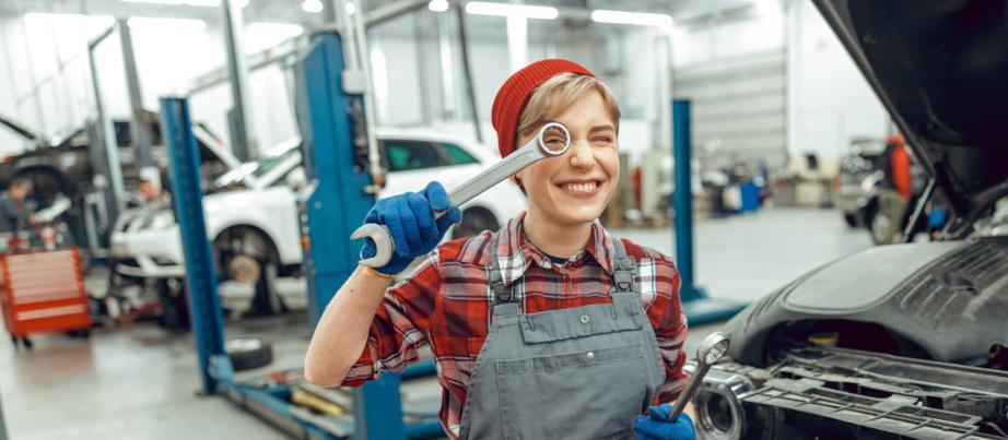 Eine Auszubildende in der Autowerkstatt hält gut gelaunt einen Schraubschlüssel vors Auge.