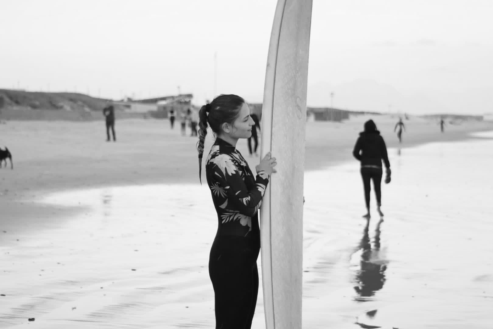 Hanna am Strand mit einem Surfboard. Sie ist kurt davor surfen zu gehen.