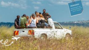 Eine Gruppe deutscher und ugandischer Jugendlicher fährt auf der Ladefläche eines Trucks über ein Feld.
