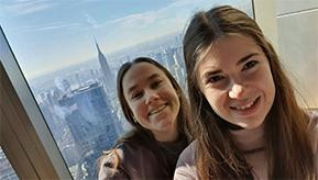 Foto: Eva und Luisa stehen vor einem Fenster, im Hintergrund sieht man das Empire State Building