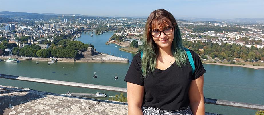 Foto: Anastassia trägt ein schwarzes Tshirt und lehnt an einem Betongeländer. Im Hintergrund sieht man den Ohrid See von oben